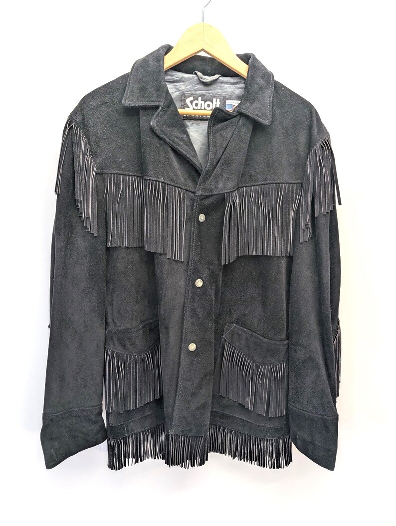 May include: Black suede jacket with fringe detailing. The jacket has a classic collar, button closure, and two front pockets. The brand name "Schott" is visible on the label. The fringe is along the chest, pockets, and sleeves.