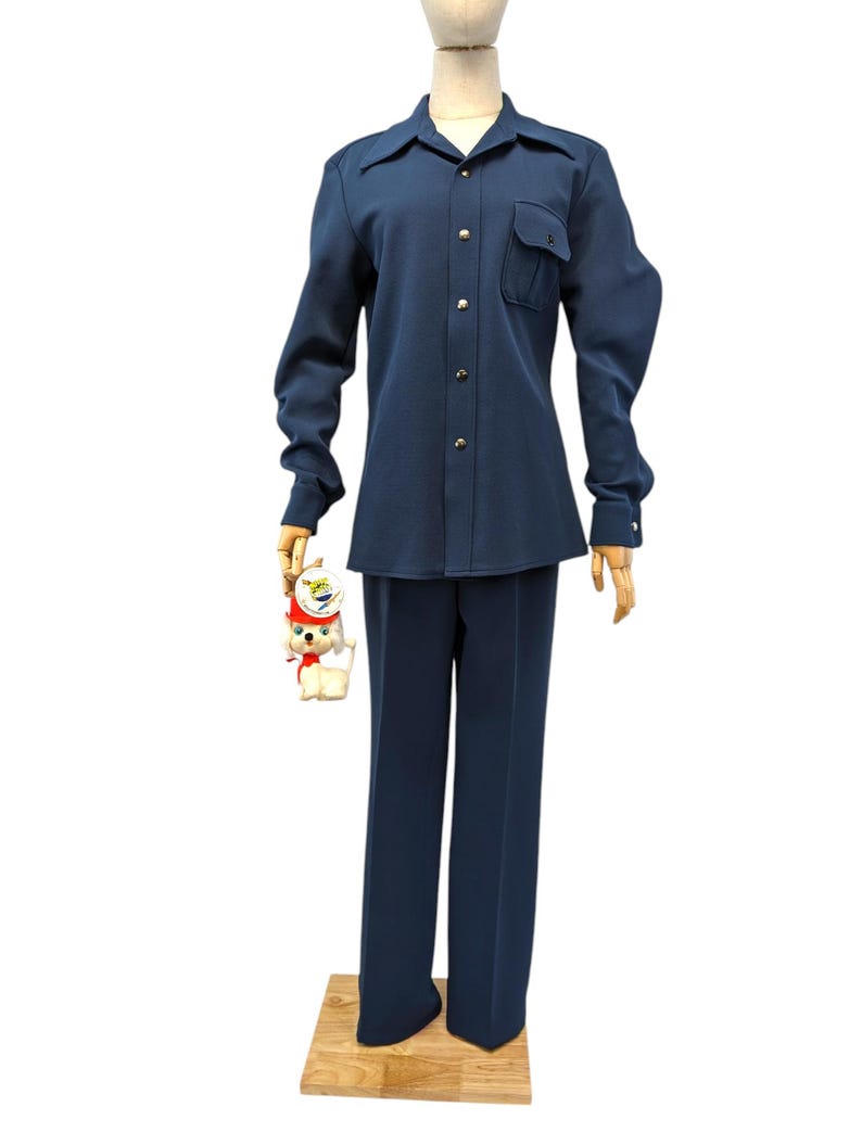 Puede incluir: Una camisa azul marino de manga larga con cuello abotonado y un solo bolsillo en el pecho izquierdo. La camisa se combina con pantalones azul marino a juego.