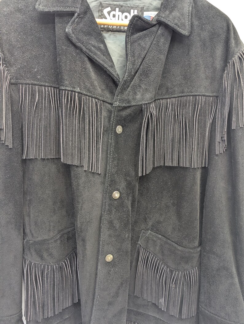 May include: Black suede jacket with fringe detailing across the chest, pockets, and sleeves. The jacket has a button-up front and a collar. The brand name "Schott" is visible on the label.
