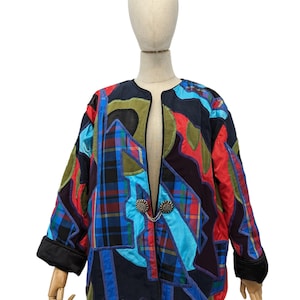 May include: A colorful, quilted jacket with a unique patchwork design. The jacket features a mix of plaid, solid, and patterned fabrics in shades of blue, red, green, and black. It has a round collar, three-quarter sleeves, and decorative clasps.