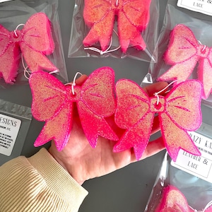 May include: Four pink and gold glitter bow-shaped car air fresheners with the text "KRAZY K" and "LEATHER & LACE" on the packaging.