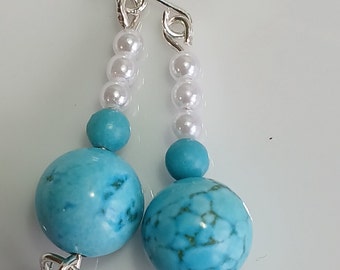 Op de afbeelding: Turquoise en witte kralen oorbellen met zilveren haakjes. De oorbellen hebben grote turquoise kralen en kleinere witte kralen.