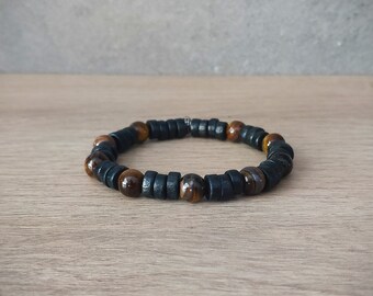 Puede incluir: Un brazalete de cuentas marrones y negras con un cierre plateado. El brazalete está hecho de cuentas redondas y está sobre una superficie de madera.