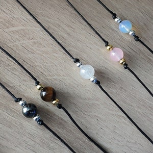 May include: Five black cord necklaces with different colored gemstone beads. The beads are a light blue, pink, brown, and black.