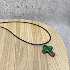 Peut inclure: Un collier avec un pendentif en forme de croix en pierre précieuse verte et rose sur un cordon en cuir noir.