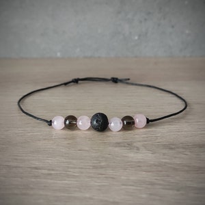May include: A black cord necklace with pink and brown beads, including a black lava rock bead.