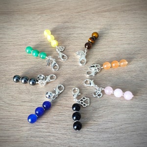 Puede incluir: Siete llaveros de cuentas de colores con dijes de plata. Los dijes incluyen una cruz, un corazón con las palabras "Dog Mom", una huella de pata, un número "3" y una pequeña figura de animal. Las cuentas son verdes, amarillas, marrones, naranjas, rosas, azules y negras.