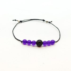Może przedstawiać: Bransoletka ze sznurka czarnego z fioletowymi koralikami i czarnym koralikiem z lawy.
