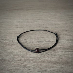 May include: A simple black cord bracelet with a single dark red gemstone bead.