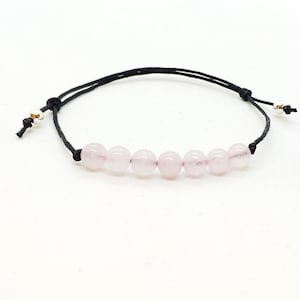 Op de afbeelding: Een armband met roze rozenkwarts kralen, een zwart koord en zilveren metalen accenten.