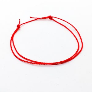 May include: A red string bracelet with a simple knot design.