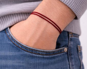 Puede incluir: Una pulsera minimalista que consta de dos finos cordones de color rojo oscuro que se llevan alrededor de la muñeca. La pulsera presenta un diseño sencillo y liso hecho de hilo fino y duradero, ofreciendo un accesorio sutil y discreto.