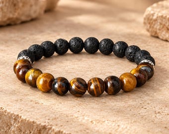 Puede incluir: Una pulsera de cuentas que combina cuentas redondas de piedra de lava negra porosa y cuentas de ojo de tigre de color marrón dorado, lisas y pulidas. Las dos secciones de cuentas están separadas por pequeños espaciadores metálicos plateados.