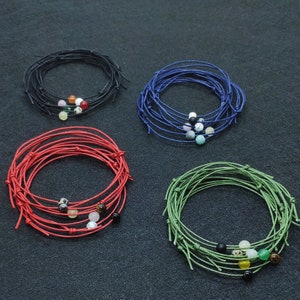 May include: Four bracelets made of multiple strands of string with different colored beads. The bracelets are black, red, blue, and green.