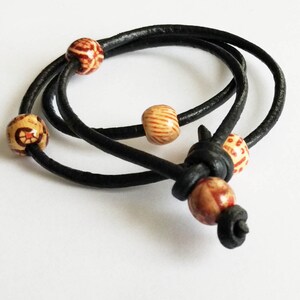May include: A black leather bracelet with four wooden beads. The beads are a light brown colour with red and orange patterns.