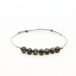 Puede incluir: Un brazalete de cuerda gris con seis cuentas redondas de color gris oscuro.