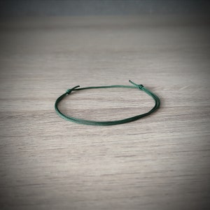Può includere: Un braccialetto in corda verde scuro con una semplice chiusura a nodo.
