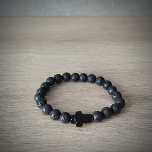 Peut inclure: Bracelet en perles de roche volcanique noire avec un pendentif en forme de croix noire.