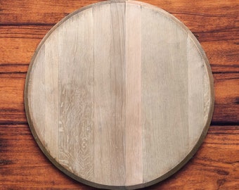 May include: A round wooden cutting board with a light brown finish. The board has a natural wood grain pattern and is made of solid wood.