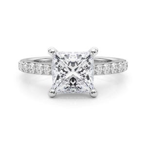 May include: A diamond engagement ring with a square-cut center stone. The ring features a band with small, round accent diamonds. The center stone is held in place by four prongs.