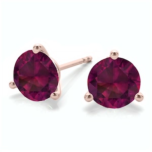 May include: A pair of rose gold stud earrings with a round, deep red gemstone in each earring.