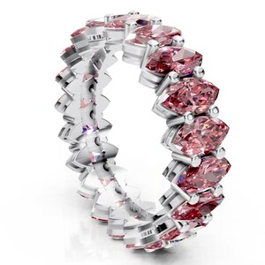 May include: A silver ring featuring a continuous row of marquise-cut pink gemstones. The gemstones are set in a channel setting, creating a seamless band of color. The ring's band has a unique, textured design.