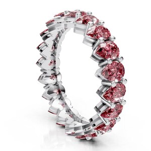 May include: A silver ring featuring a continuous row of pink pear-shaped gemstones. The gemstones are set closely together, creating a full band of color. The ring is set against a white background.