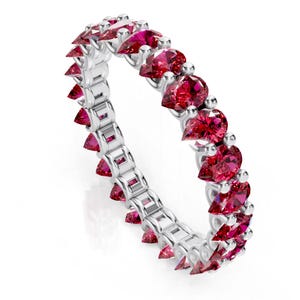 May include: A silver ring featuring a continuous row of vibrant red pear-shaped gemstones. The ring's band has a unique design with triangular red gems. This elegant piece of jewelry is perfect for special occasions.