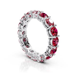 May include: A silver eternity ring featuring a continuous row of oval-cut, vibrant red gemstones. The gemstones are set in individual prongs, creating a sparkling and elegant design. This ring is a classic piece of jewelry.