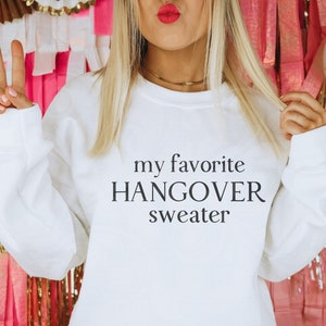 Puede incluir: Sudadera blanca con el texto "my favorite hangover sweater" impreso en la parte delantera.