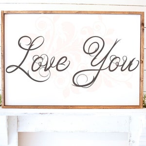 May include: A white wooden sign with a brown frame featuring the words "Love You" in a decorative script font.