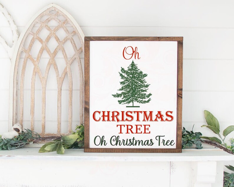 May include: A wooden sign with a white background and brown frame. The sign features a green Christmas tree illustration and the text "Oh Christmas Tree Oh Christmas Tree" in red.