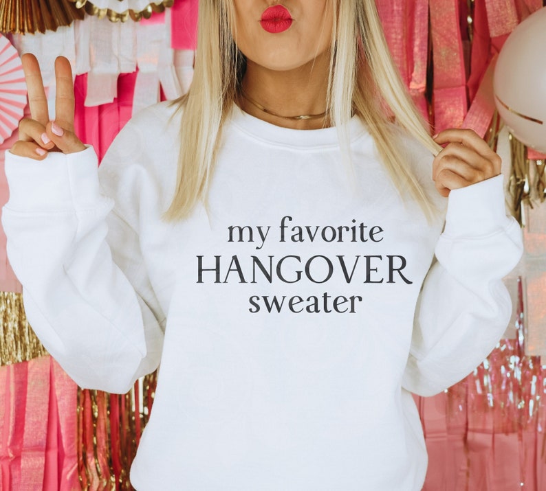 Puede incluir: Sudadera blanca con el texto "my favorite hangover sweater" impreso en la parte delantera.