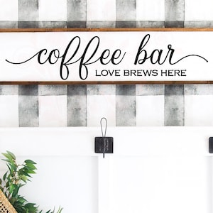May include: A wooden sign with the text "coffee bar" in a cursive font and the words "Love brews here" in a smaller font below. The sign is hanging on a wall with a black and white checkered pattern.