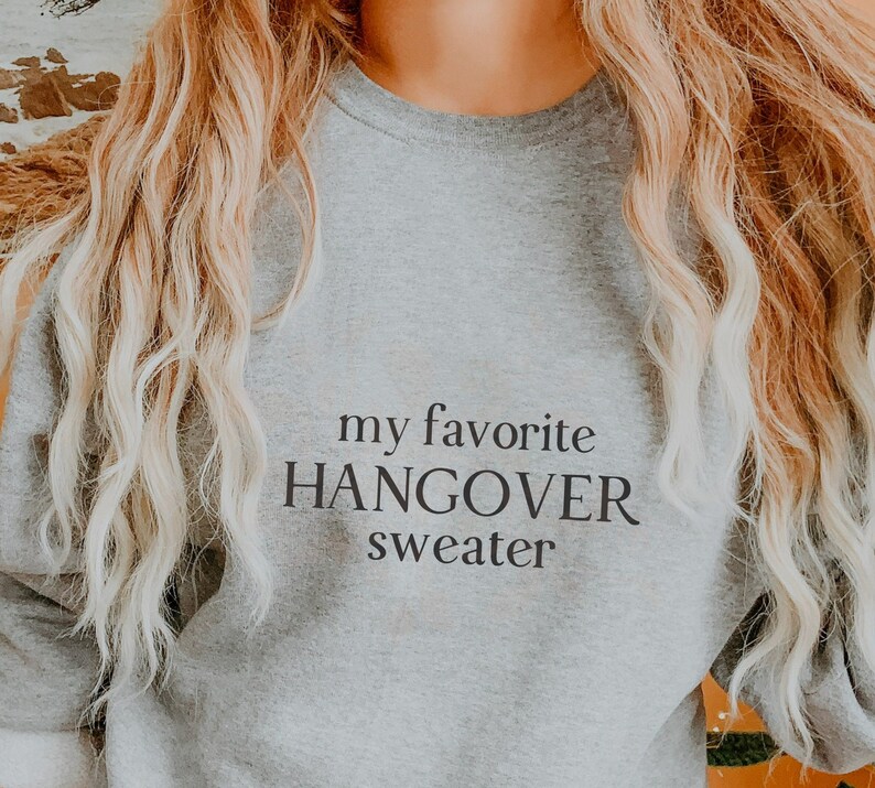 Puede incluir: Una sudadera gris con el texto "my favorite HANGOVER sweater" impreso en la parte delantera.