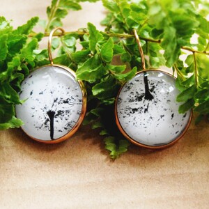 May include: A pair of gold hoop earrings with round glass pendants featuring a black and white dandelion design.