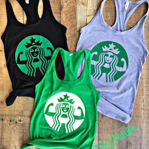 Pode incluir: Três regatas nas cores verde, preto e cinza. Cada regata apresenta um gráfico branco de uma mulher com uma coroa e bíceps musculosos, que se assemelha ao logotipo da Starbucks.