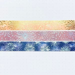 May include: Three rolls of washi tape with a firework pattern. The top roll is peach with gold glitter, the middle roll is pink with silver glitter, and the bottom roll is blue with silver glitter.