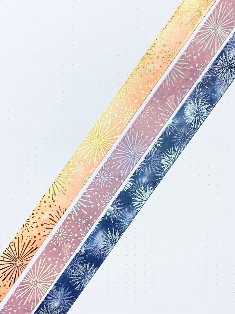 May include: Three rolls of washi tape with a firework design. The tape is in shades of blue, pink, and orange.