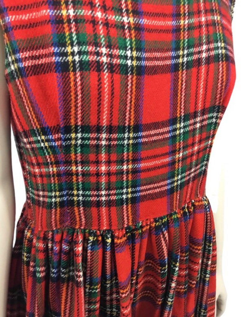 May include: Red plaid dress with a gathered skirt. The dress has a sleeveless design and a classic plaid pattern.