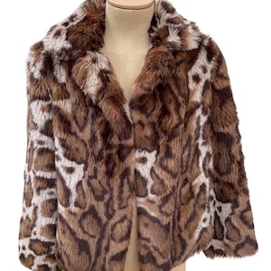 May include: A faux fur coat with a brown, tan, and white animal print pattern. The coat has a wide collar and is displayed on a mannequin. The coat is open in the front.