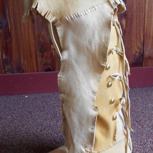 May include: A pair of tan leather moccasins with a fringe detail and a lace-up design. The moccasins have a pointed toe and a flat sole.