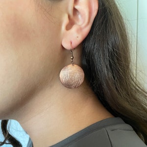 May include: A pair of copper earrings with a brushed finish. The earrings are round and have a simple design.