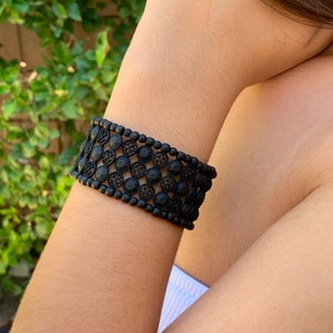 May include: A black beaded bracelet with a delicate lace design and black rhinestones.