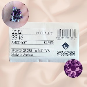Könnte beinhalten: Nahaufnahme einer Packung mit 1.440 amethystfarbenen Swarovski-Kristallen in Größe SS16. Die Packung ist mit "2012", "SS 16", "Amethyst", "1. Qualität", "Silber", "10/00/00 Brutto = 1.440 STK.", "Hergestellt in Österreich" und "Swarovski Components" beschriftet.