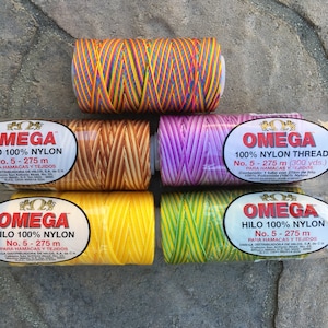 May include: Six spools of colorful nylon thread for making hammocks and other crafts. The spools are labeled "OMEGA 100% NYLON" and have different color combinations, including rainbow, brown and yellow, purple and white, yellow and green, and yellow and orange.
