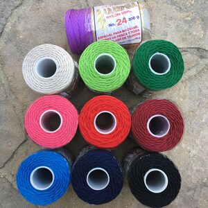 May include: Ten spools of nylon cord in various colors, including purple, white, green, red, pink, dark red, blue, navy blue, and black. Each spool is labeled "La Espiga Nylon 100% No. 24 200 g".