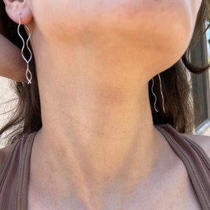 May include: A pair of silver wavy earrings. The earrings are long and thin, and they have a delicate, flowing design.