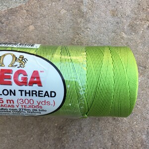 May include: A spool of bright green nylon thread labeled "Omega Nylon Thread 5m (300 yds.) Lacas y Tejidos  ubo con 275m de hilo mida (100% Nylon) Mexico/Made in Mexico"
