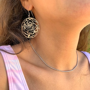 May include: A pair of gold-toned earrings featuring a delicate rose design. The earrings are circular and have a cutout pattern that resembles a rose.